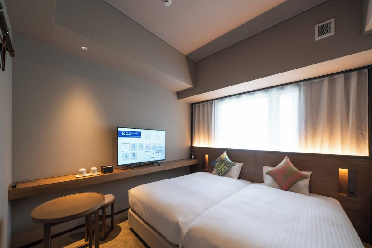 A hotel room with a bed, a desk, and a television displaying a digital interface.
