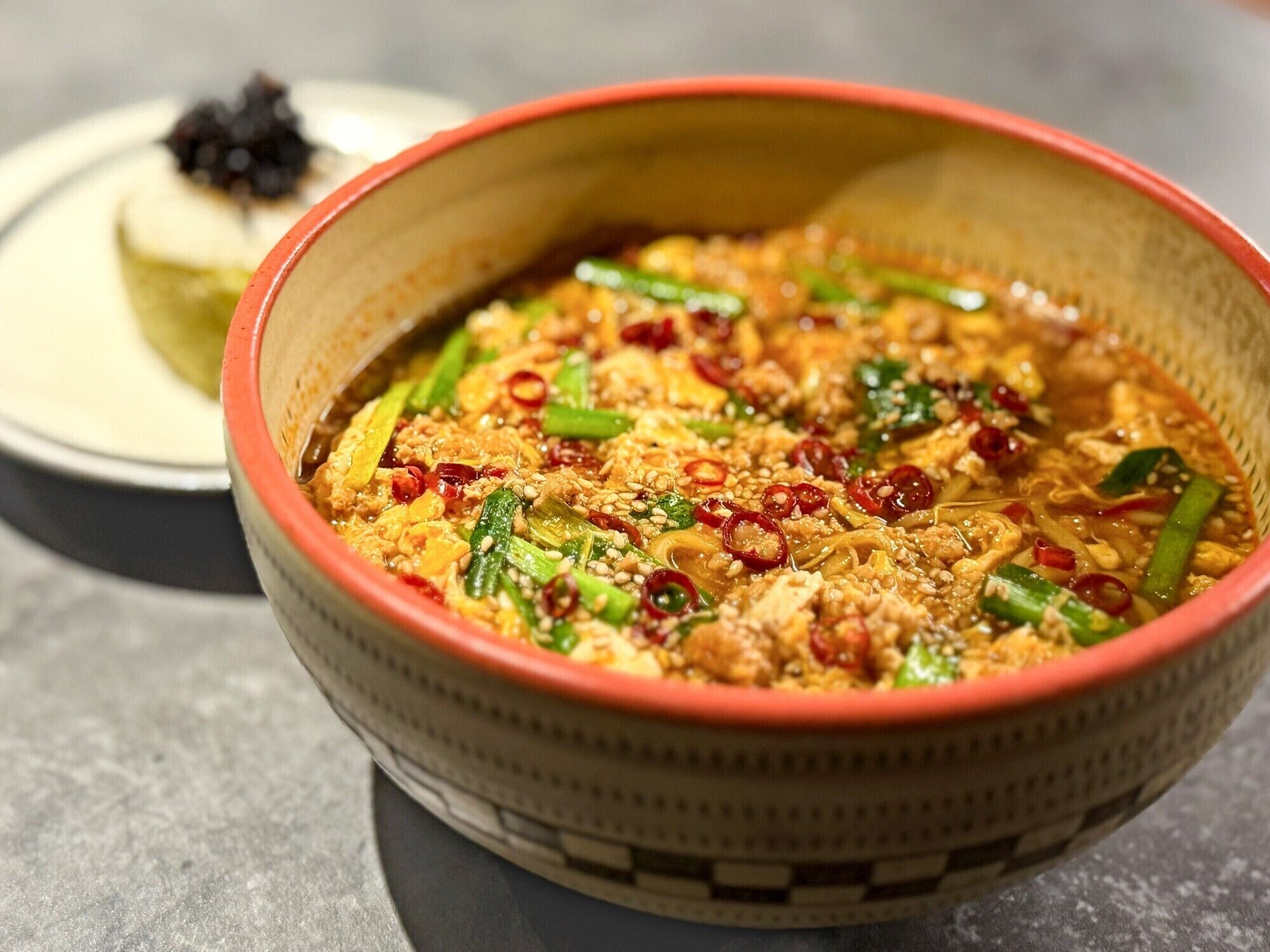 A bowl of Asian noodle soup with vegetables and meat, served in a woven bowl.
