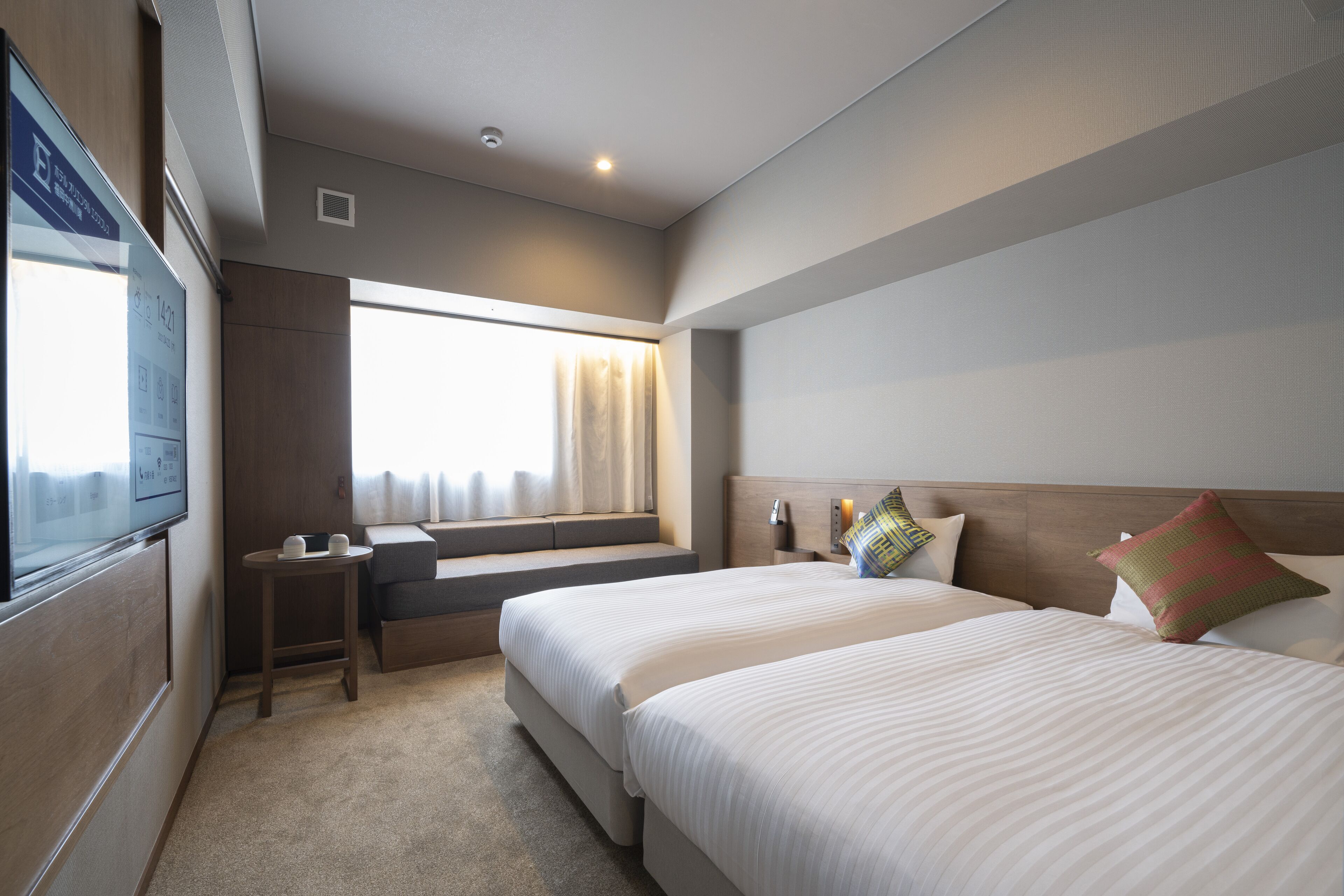 A hotel room with two beds, a TV, a window with curtains, and a small table.