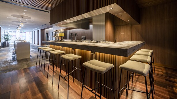 Un área de bar moderna con una barra larga, varios taburetes y una cocina amplia al fondo.