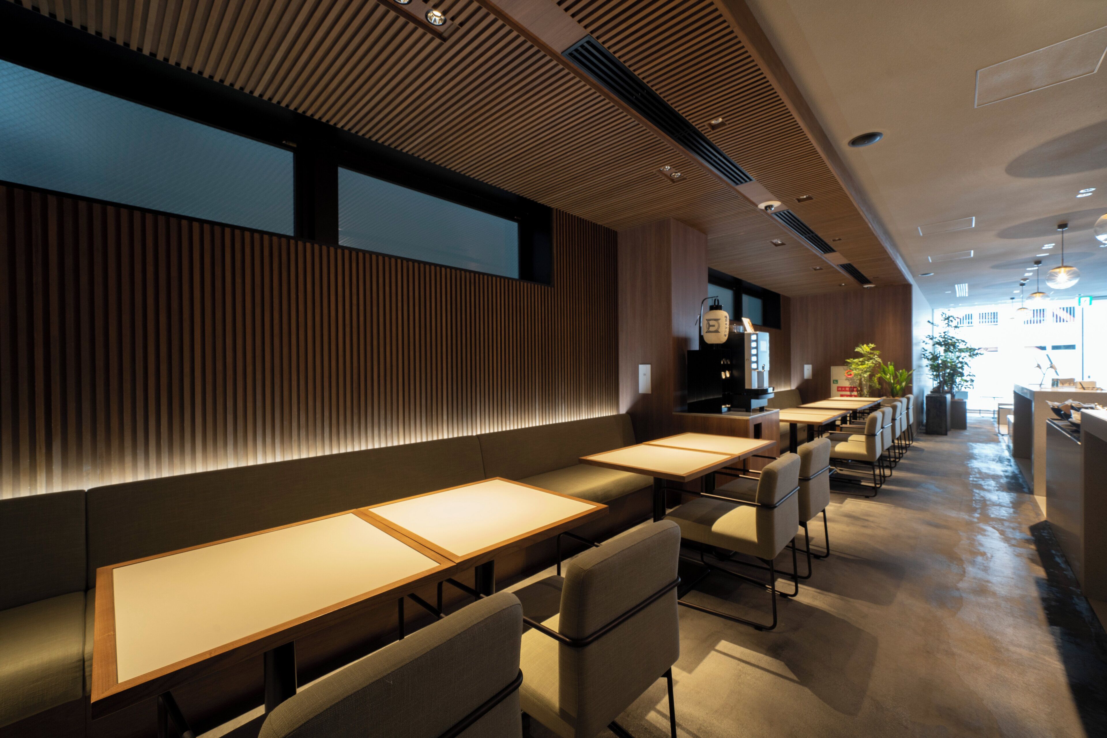 A modern restaurant interior with long communal tables, cushioned seating, and a wooden accent wall.