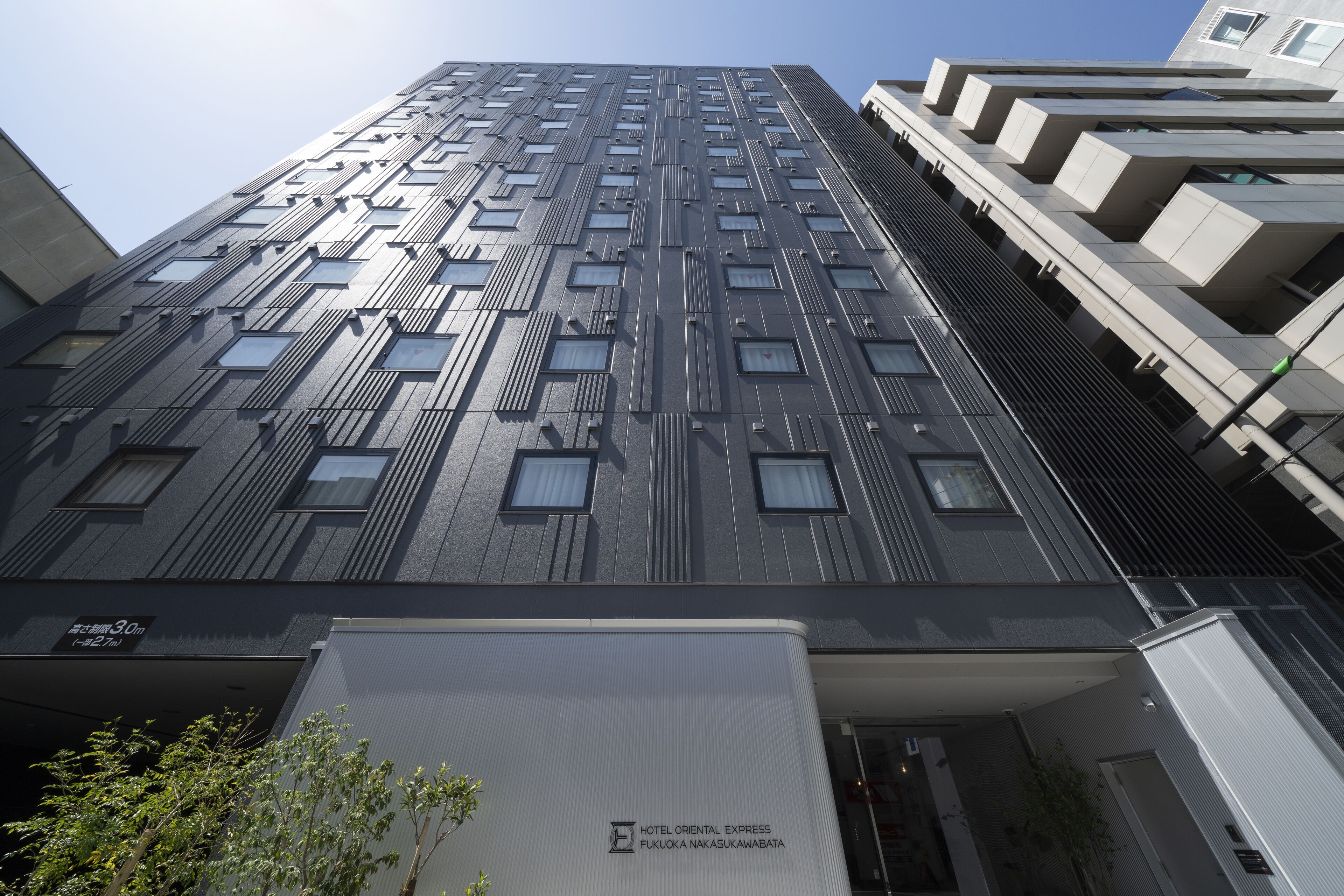 A modern hotel building with a vertical design, multiple windows, and a sign indicating it is the Hotel Oriental Express Fukuoka Nakasu Kawabata.
