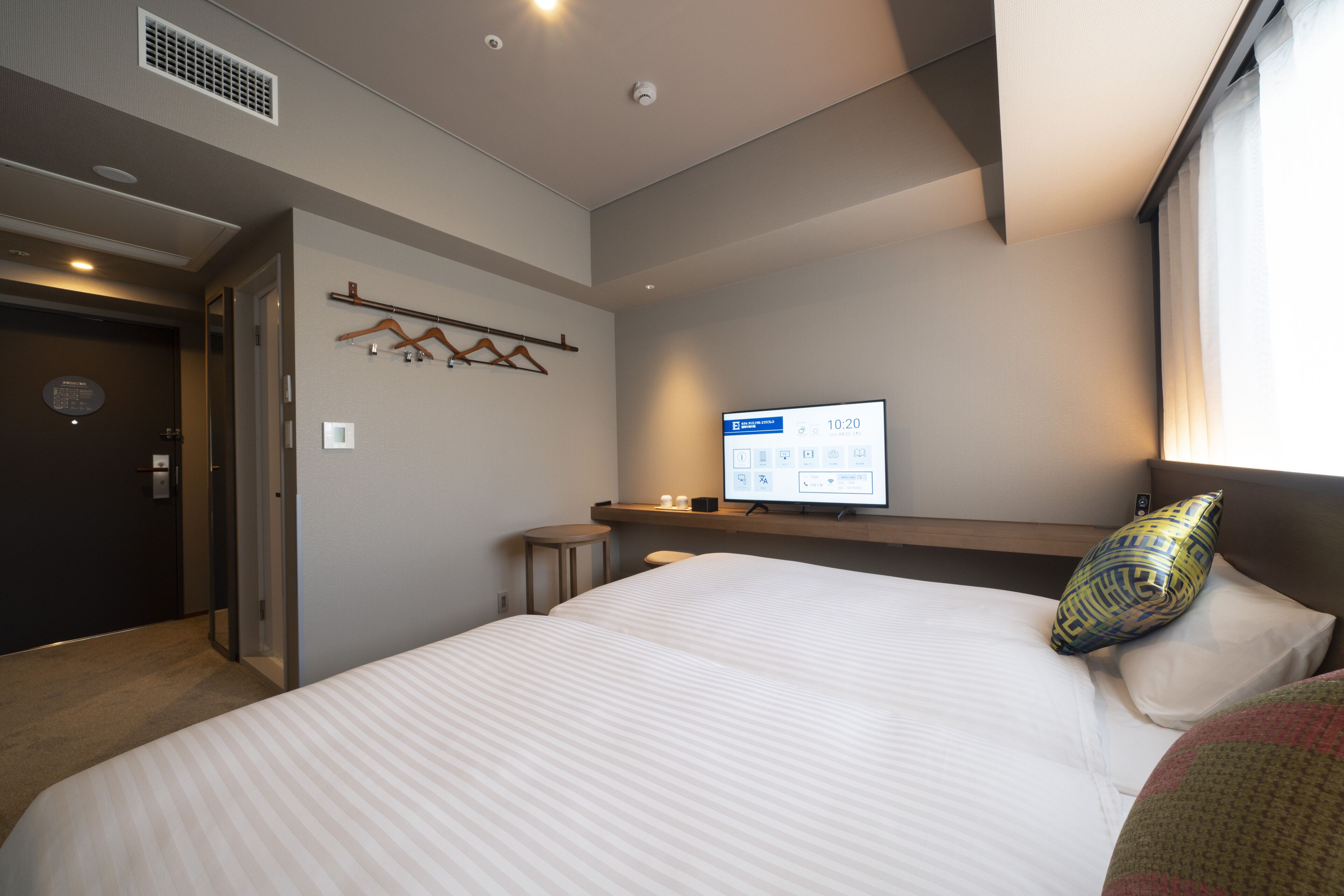 A hotel room with a large bed, a bedside table, a TV, and a window with curtains.