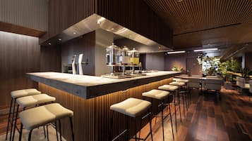 A modern bar area with a wooden bar counter, stools, and a seating area with tables and chairs.