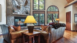 Ein gemütliches Wohnzimmer mit Kamin aus Stein, Ledersofas und großen Fenstern mit Blick ins Freie.