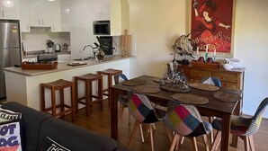 Una cocina moderna con armarios blancos, horno empotrado y un comedor con mesa de madera y sillas coloridas.