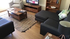 Una sala de estar con televisión, sofá, sillón, mesa de centro, estantería y un juego de ajedrez.
