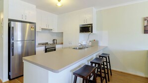 Una cocina moderna con armarios blancos, un refrigerador de acero inoxidable, un microondas, una estufa y un lavamanos. Hay tres taburetes de madera en la isla.