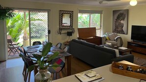 Una sala de estar con sofá, televisor, ventilador de techo y comedor con sillas y mesa.