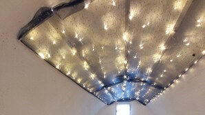A bedroom with a wooden bed, a small window, and a ceiling with string lights.