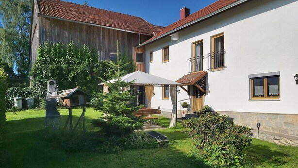 A two-story house with a red-tiled roof, a white exterior, and a small balcony.
