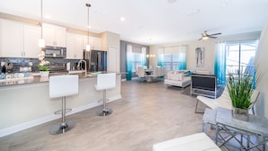 A modern kitchen with a central island, bar stools, and a dining area with a sofa and table. - MO4393 Storey Lake Condo  5Beds 4Baths Private Pool and Free Waterpark (Kissimmee)