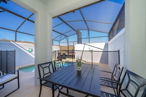 A covered outdoor patio with a pool, a table, and chairs.