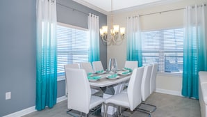 A dining room with a round table, white chairs, teal curtains, and a chandelier. - MO4393 Storey Lake Condo  5Beds 4Baths Private Pool and Free Waterpark (Kissimmee)