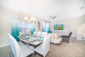 A dining area with a white table set for six, white chairs, a chandelier, and a ceiling fan.