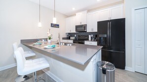 A modern kitchen with white cabinets, stainless steel appliances, a central island with bar stools, and pendant lighting. - MO4393 Storey Lake Condo  5Beds 4Baths Private Pool and Free Waterpark (Kissimmee)
