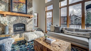 A cozy living room with a stone fireplace, large windows, a sofa, and a coffee table.