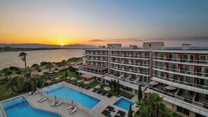 Ein Hotel mit Pool, Liegestühlen und Blick auf den Sonnenuntergang über dem Wasser.