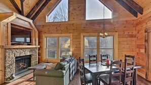 Een gezellig cabin interieur met een stenen openhaard, een bank, een eettafel en grote ramen.