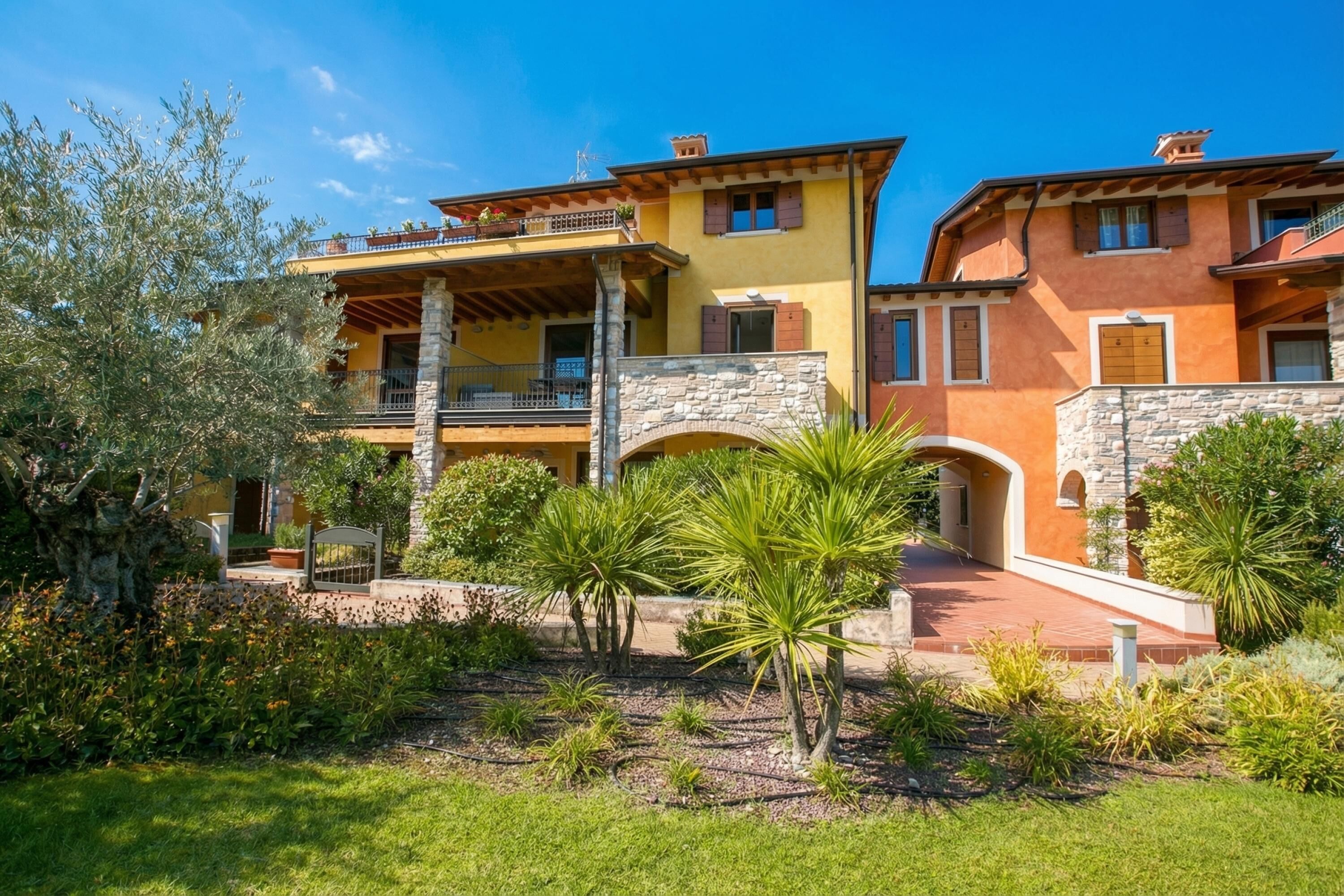 A two-story building with a stone archway, a balcony, and a garden with palm trees.