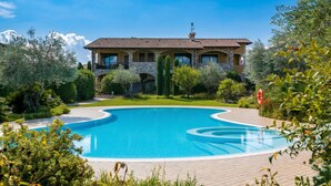 A large swimming pool with a curved design, surrounded by lush greenery and a large building with multiple balconies.
