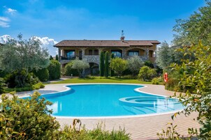 A large swimming pool with a curved design, surrounded by lush greenery and a large building with multiple balconies.