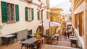 A cobblestone courtyard with outdoor seating, a street lamp, and buildings with green shutters.