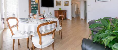 Un comedor con una mesa redonda dispuesta para cuatro personas, un televisor montado en la pared y una estantería.