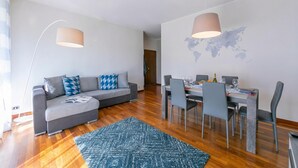 A modern living room with a sofa, dining table, chairs, and a world map on the wall. - Appartamento Il Golfo: Lake View in Laveno-mombello (Laveno Mombello)