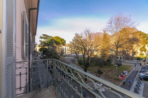 A balcony with a metal railing overlooking a street with parked cars and trees.