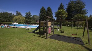 A playground with a slide and swings, a pool, and a grassy area with chairs. - Riva del Caolino (Ispra)