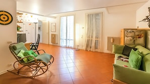 A living room with a rocking chair, a green sofa, and a dining area with a table and chairs. - Riva del Caolino (Ispra)