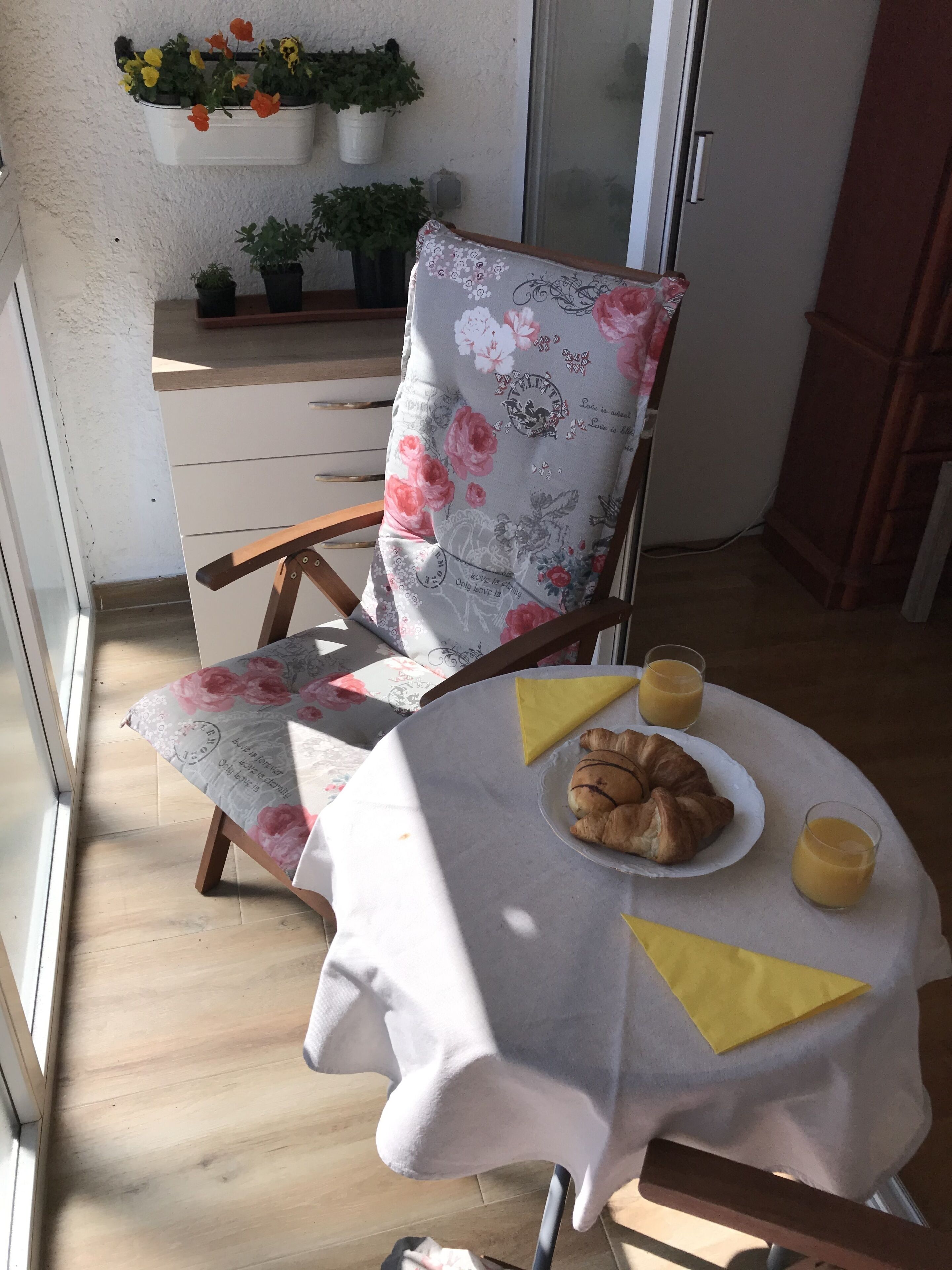 A dining area with a floral chair, a table with a white tablecloth, a plate of croissants, and two glasses of orange juice.