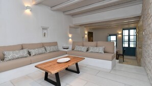 A modern living room with a large beige sectional sofa, a wooden coffee table, and a stone wall. - Sea Swell Villa 2 - stylish home with shared pool (Santa Maria)