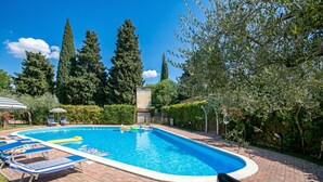 A rectangular swimming pool with lounge chairs and a flagpole, surrounded by trees and a brick pathway. - Borgo Degli Ulivi shared pool- 200m lake (Toscolano Maderno)