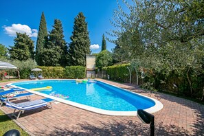 A rectangular swimming pool with lounge chairs and a flagpole, surrounded by trees and a brick pathway. - Borgo Degli Ulivi shared pool- 200m lake (Toscolano Maderno)