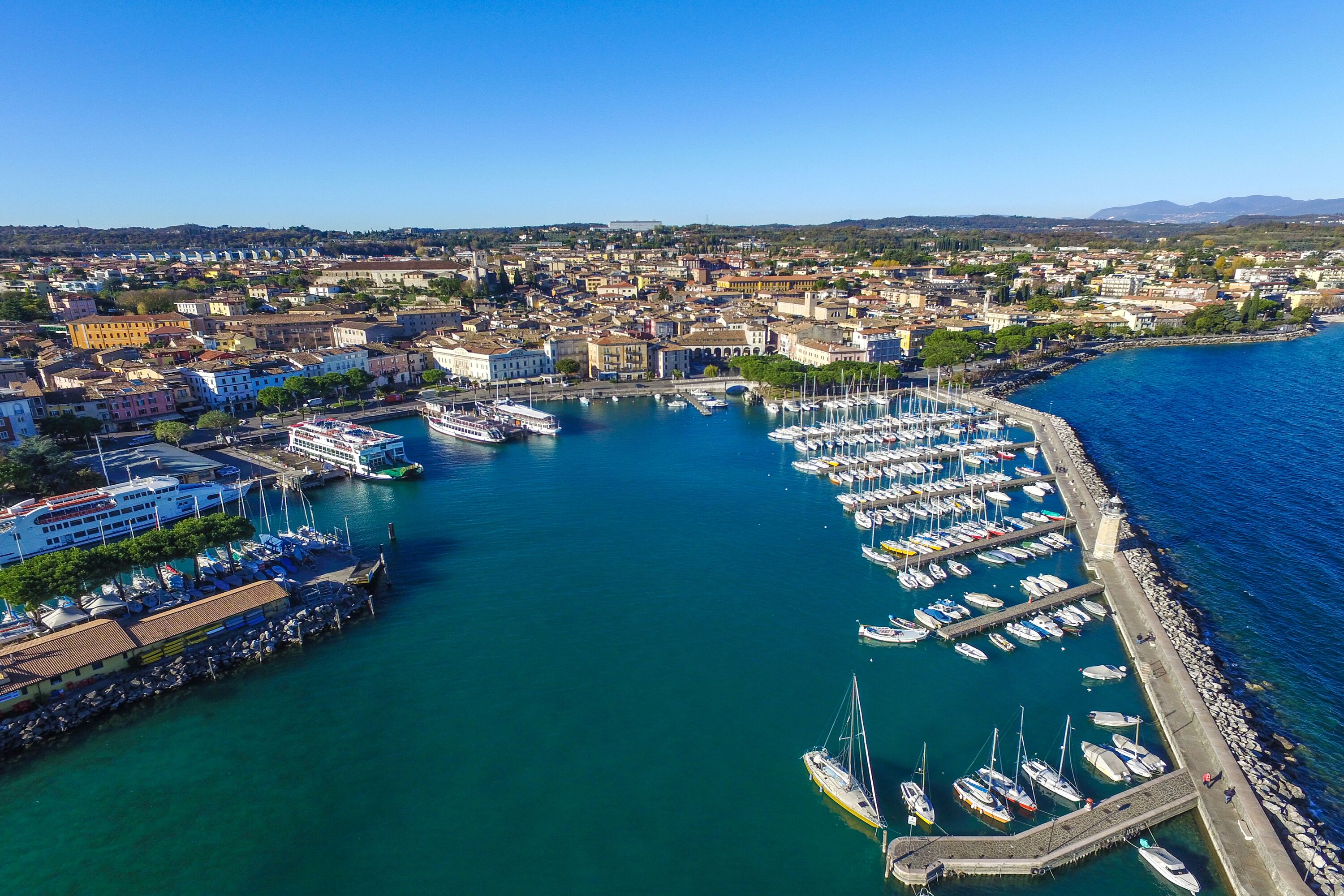 Vista aérea de un puerto deportivo con numerosos barcos amarrados, un gran crucero y un paisaje urbano al fondo.