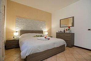 A neatly made bed with a patterned bedspread, two bedside tables with lamps, a dresser, and a mirror on the wall. - Borgo Degli Ulivi shared pool- 200m lake (Toscolano Maderno)