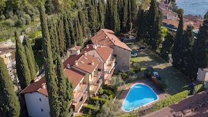 A residential area with a swimming pool, tall cypress trees, and a stone building. - Borgo Degli Ulivi shared pool- 200m lake (Toscolano Maderno)