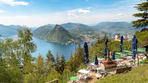 Een sfeervol buitenterrein met tafels en stoelen, met uitzicht op een meer en bergen.