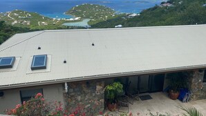 Ett hus med ett tak av metall, stenväggar och utsikt över havet och kullarna.