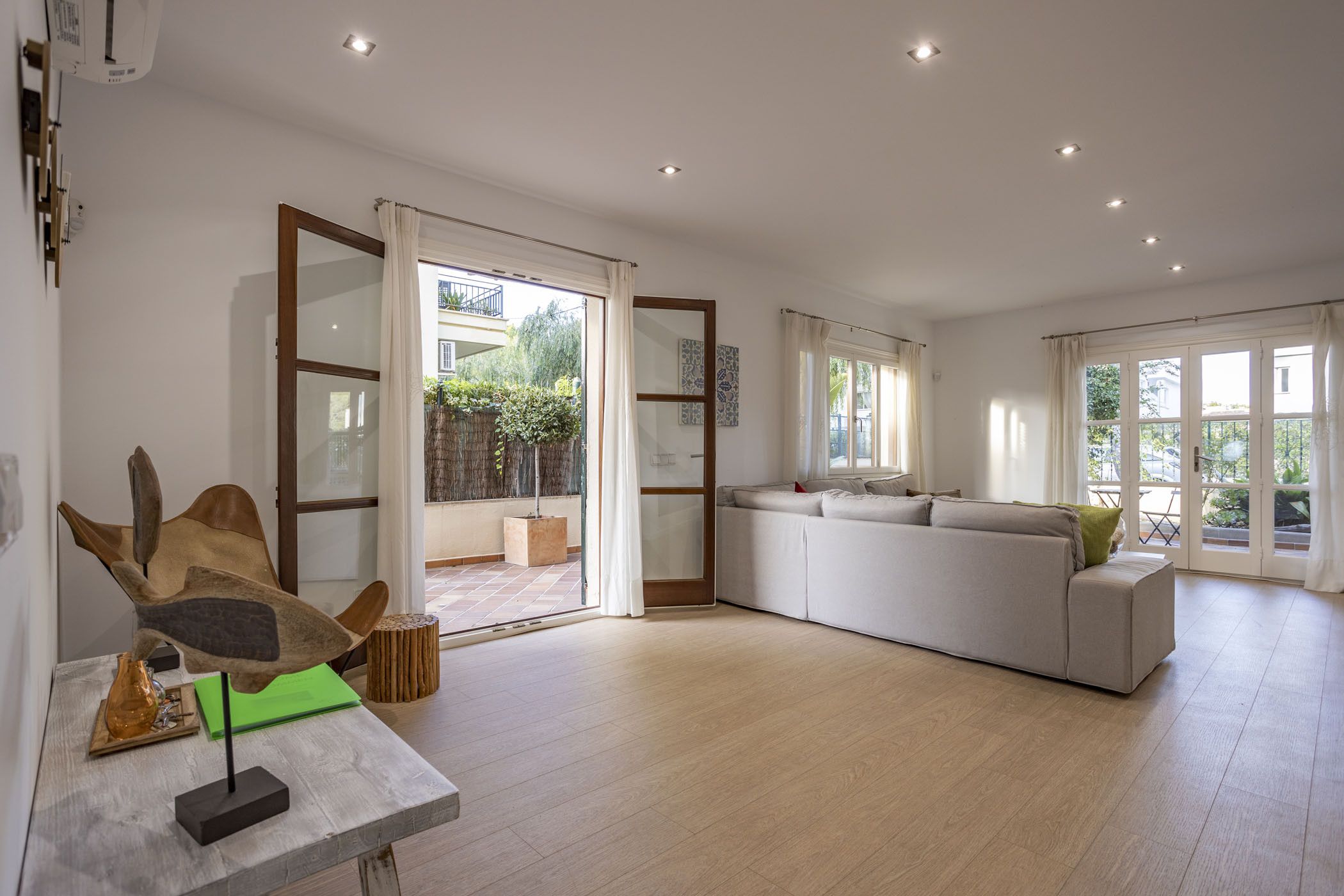 A spacious living room with a large white sofa, a wooden coffee table, and a glass door leading to an outdoor area.
