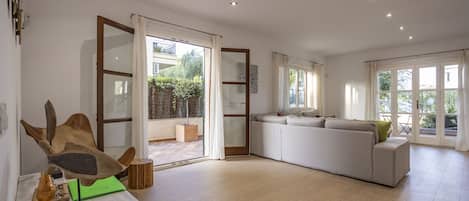 Un salón amplio con un sofá blanco grande, una mesa de centro de madera y un ventanal que da a un área exterior.