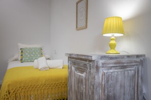 A neatly made bed with a yellow blanket and a pillow, a yellow lamp on a wooden nightstand, and a framed picture on the wall. - Modern house with 3 bedrooms, 2 bathrooms, wifi, terrace and barbecue 100 meters from the beach (Puerto de Alcudia)