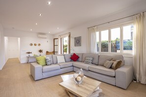 A modern living room with a grey sectional sofa, a coffee table with decorative items, and large windows with curtains. - Modern house with 3 bedrooms, 2 bathrooms, wifi, terrace and barbecue 100 meters from the beach (Puerto de Alcudia)