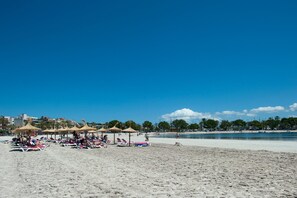 Une plage avec des transats et des parasols, un ciel dégagé et une mer calme.