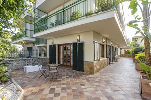 A two-story building with a tiled patio, outdoor furniture, and a balcony with green railings. - Modern house with 3 bedrooms, 2 bathrooms, wifi, terrace and barbecue 100 meters from the beach (Puerto de Alcudia)