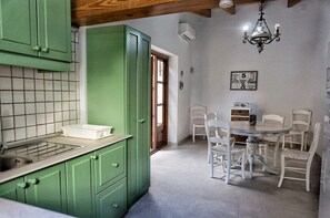 A kitchen with green cabinets, a white countertop, and a dining area with white chairs and a round table.