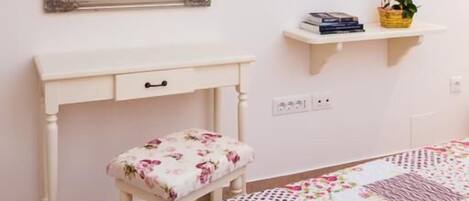 A bedroom with a bed, a bedside table, a mirror, and a small shelf with books and a plant.