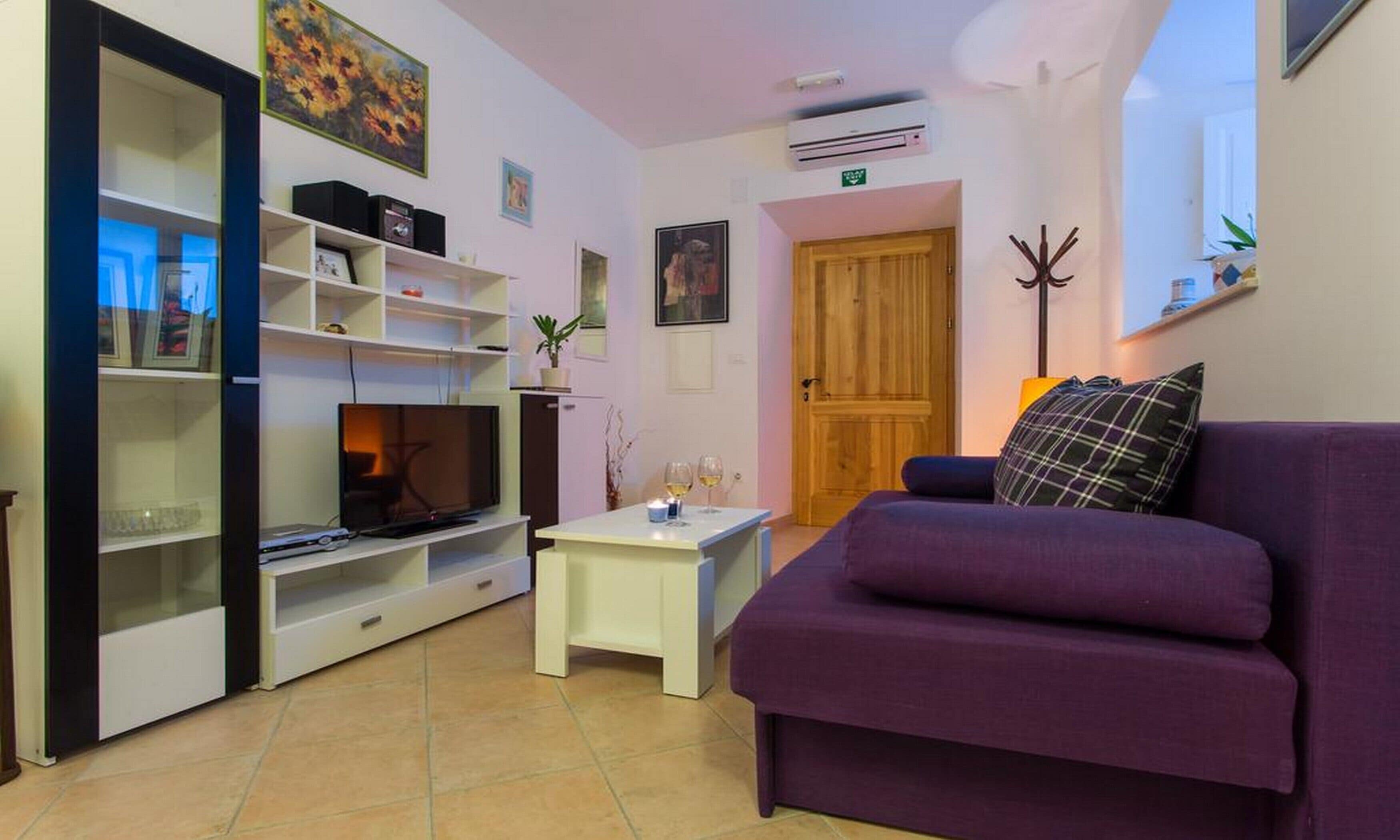 Una sala de estar con un sofá púrpura, un televisor y una mesita con vasos.